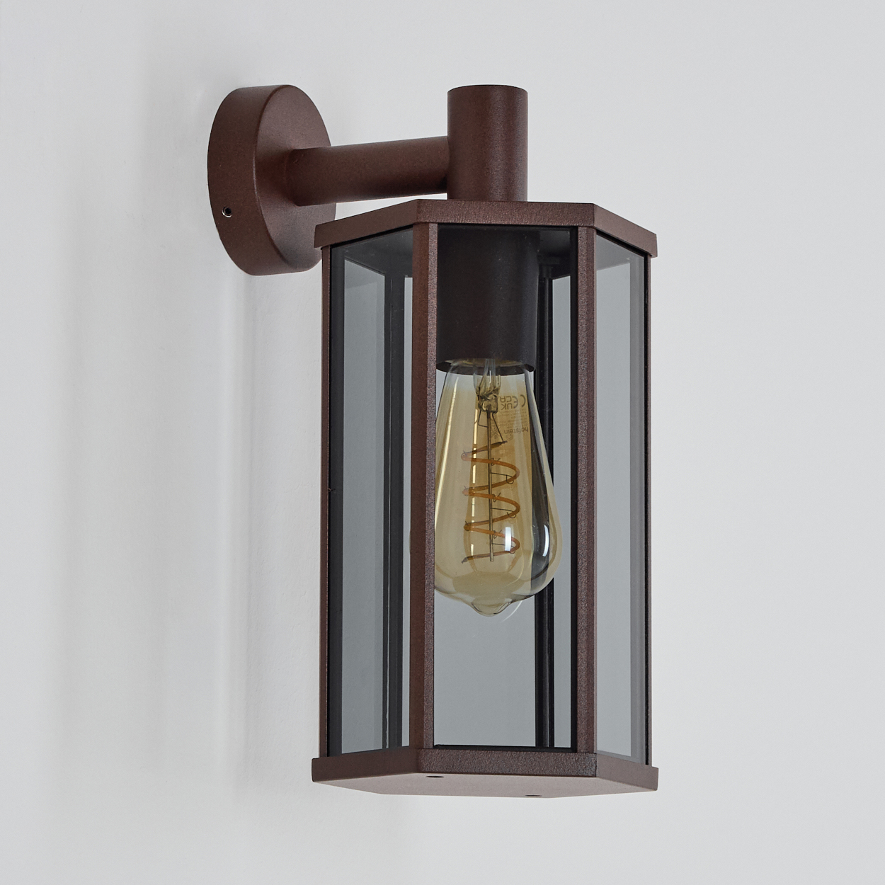 Braune Außenwandleuchte mit Glasgehäuse und sichtbarer Glühbirne an weißer Wand.