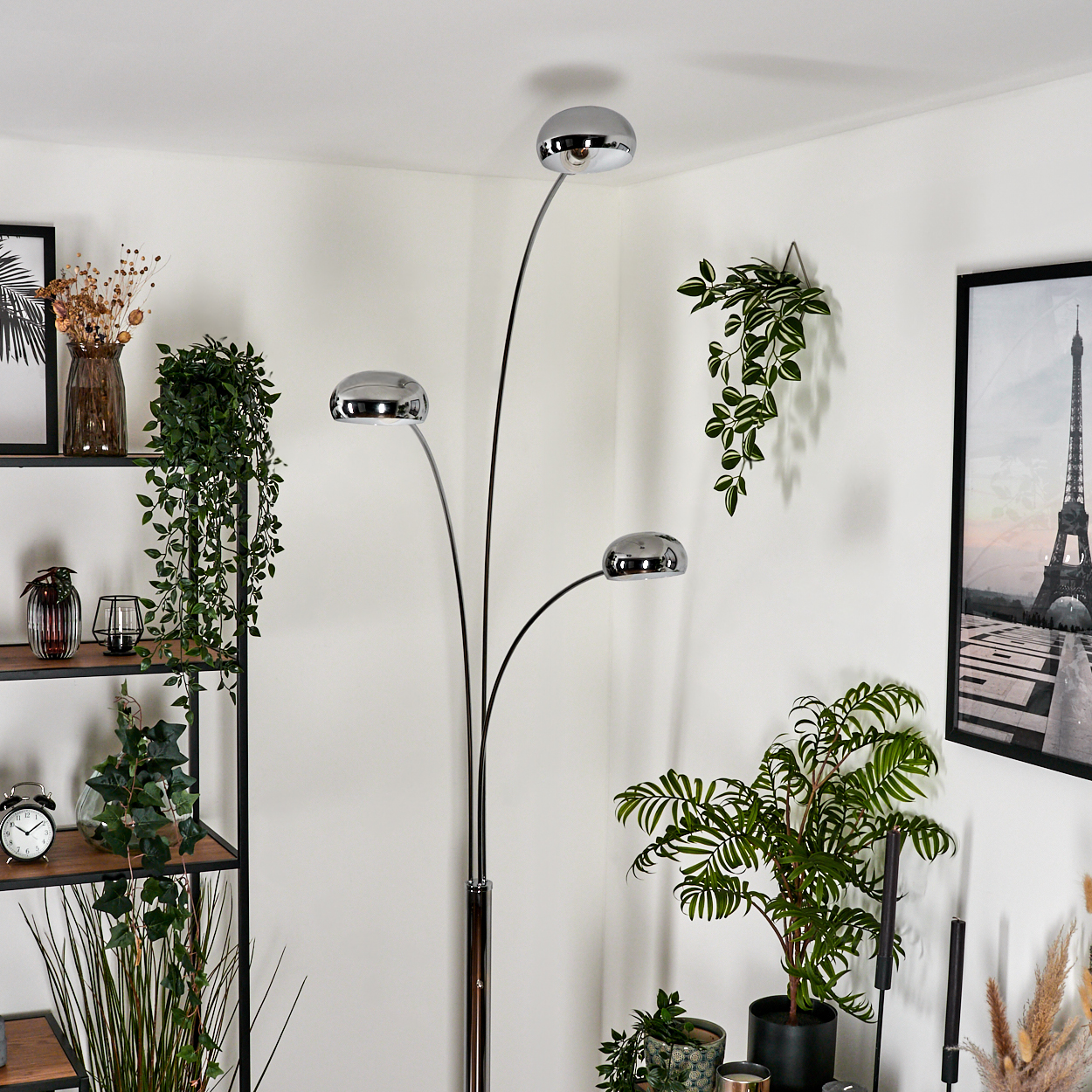 Eine dreifacharmige, verchromte Stehlampe mit drei Kugeln, in einem Raum mit Pflanzen und Dekoration.