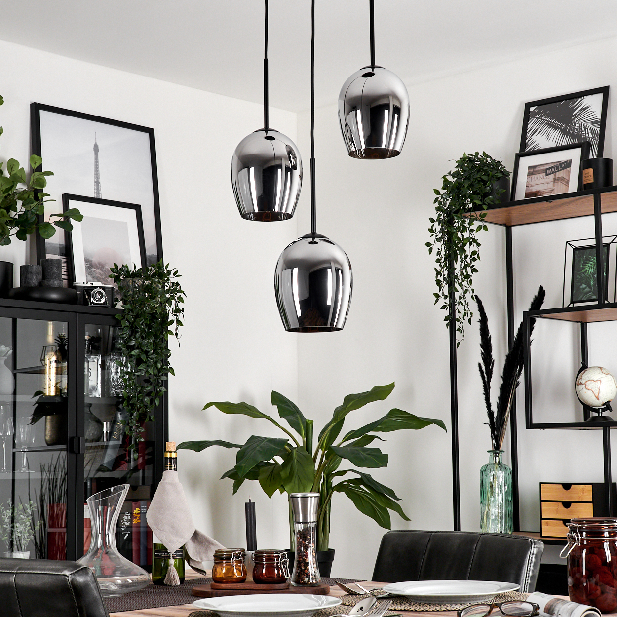 Drei Chrom-Pendelleuchten hängen in einem Esszimmer. Der Raum hat Dekoration und Pflanzen.