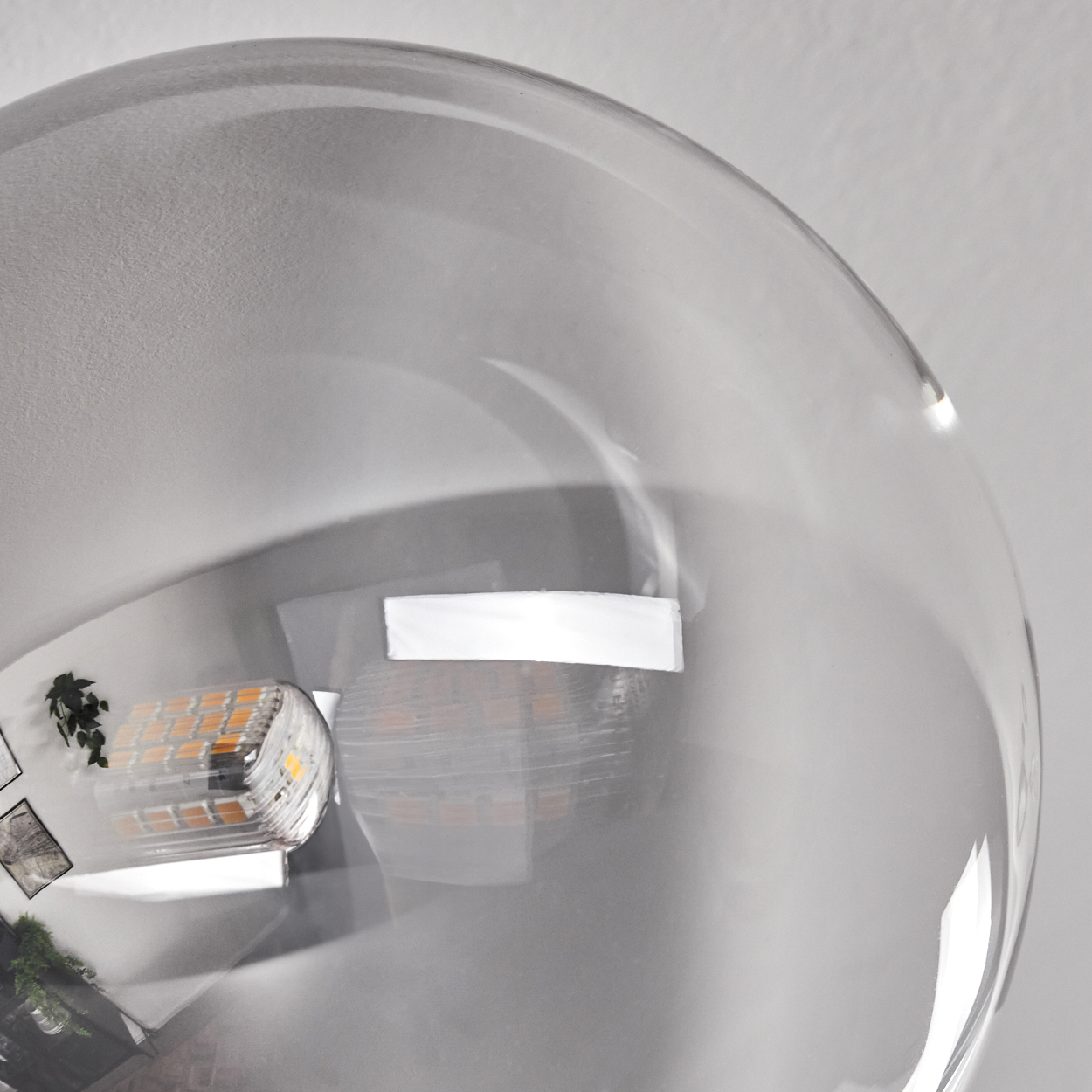 Nahaufnahme einer transparenten, kugelförmigen Leuchte mit sichtbarer LED-Lichtquelle im Inneren, an einer Decke montiert.
