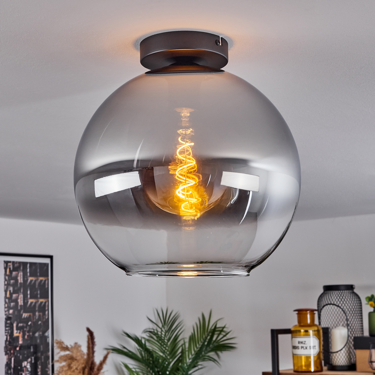 Eine Deckenlampe mit silberfarbener Glühbirne. Der Raum hat Pflanzen und Dekorationen.
