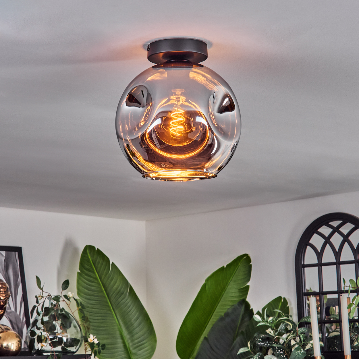 Eine kugelförmige Leuchte mit sichtbarer Glühbirne hängt von einer Decke. Die Glühbirne strahlt warmes, orangefarbenes Licht aus.
