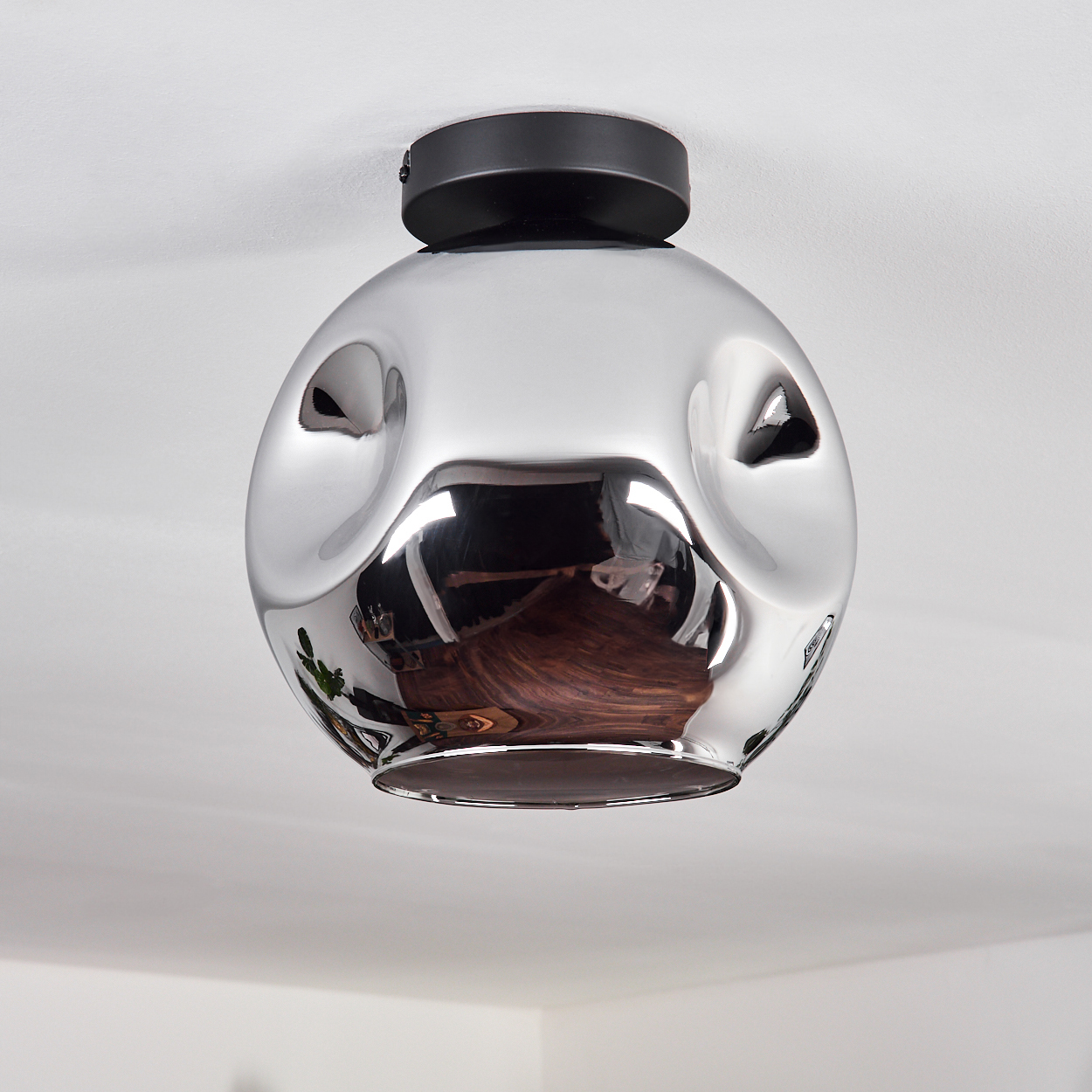 Eine runde, silberne Deckenlampe. Die Lampe reflektiert die weiße Decke.