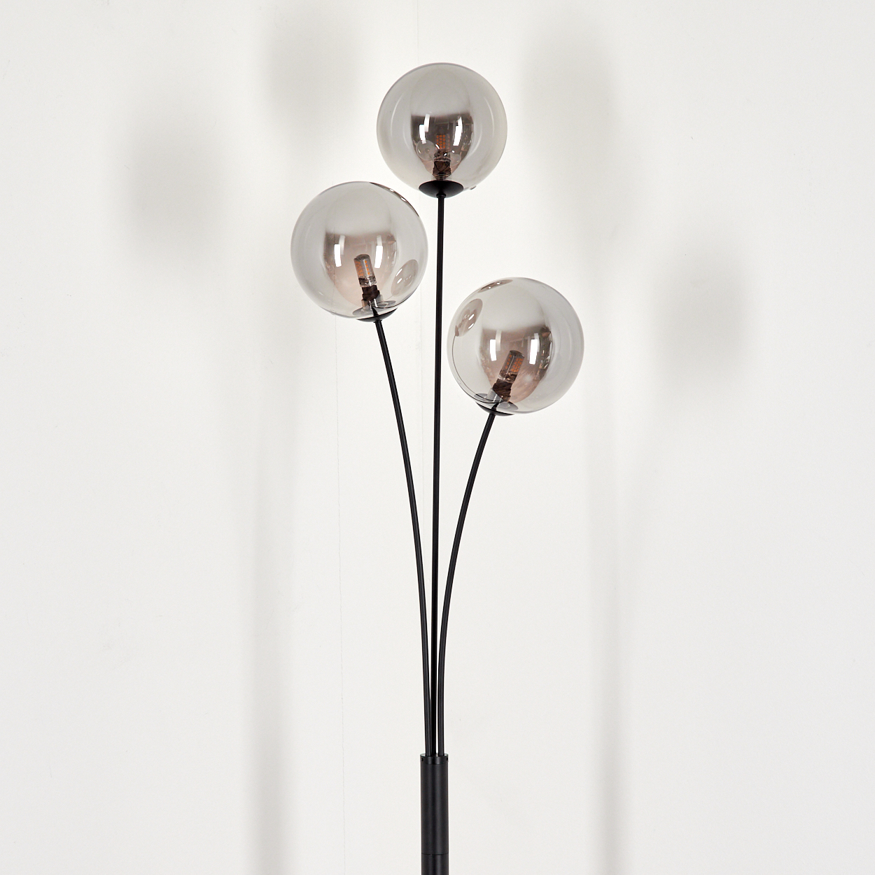 Eine Stehlampe mit drei Glaskugelschirmen. Sie steht auf weißem Hintergrund.