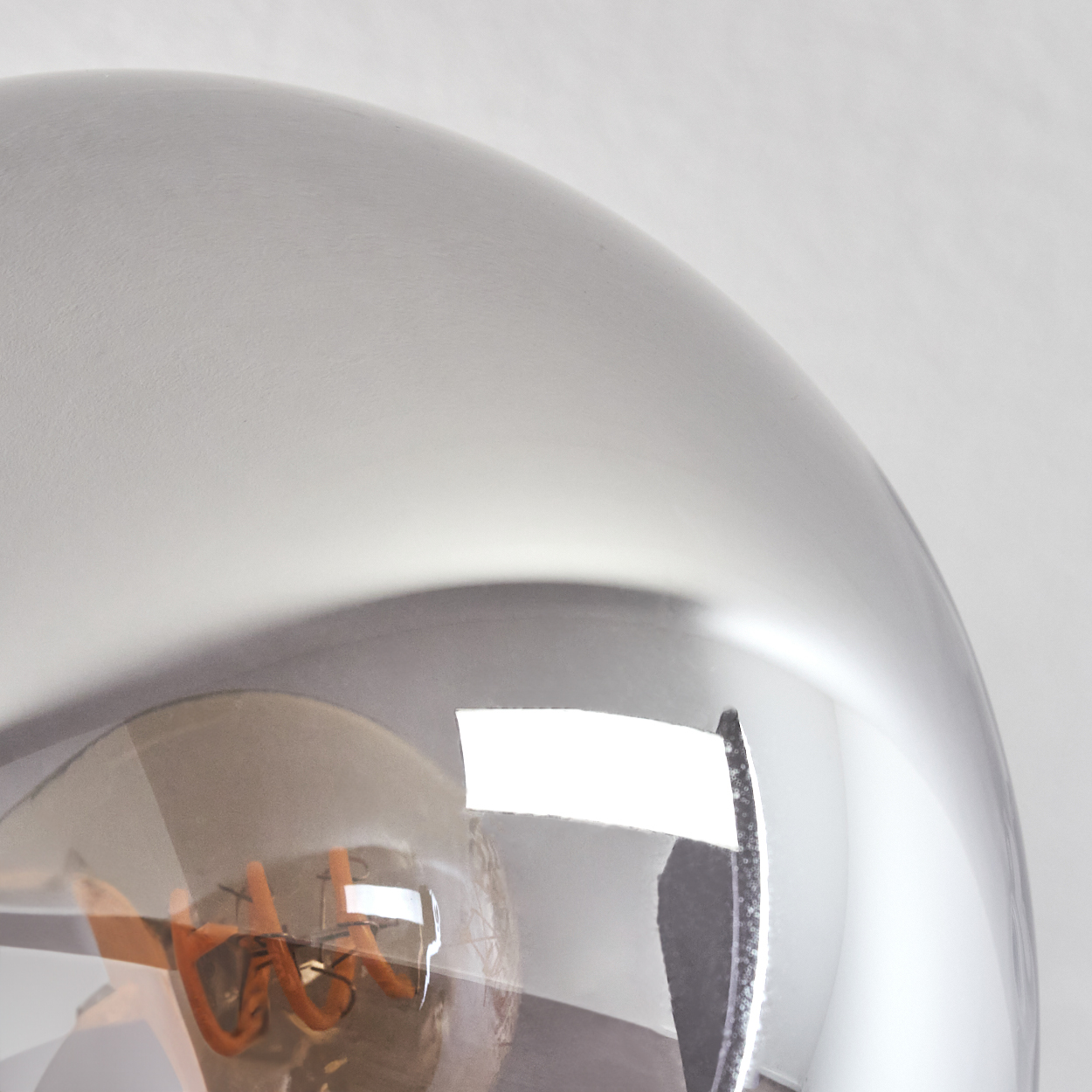 Nahaufnahme einer reflektierenden, runden Lampe mit glühendem Glühfaden. Vor weißem Hintergrund.