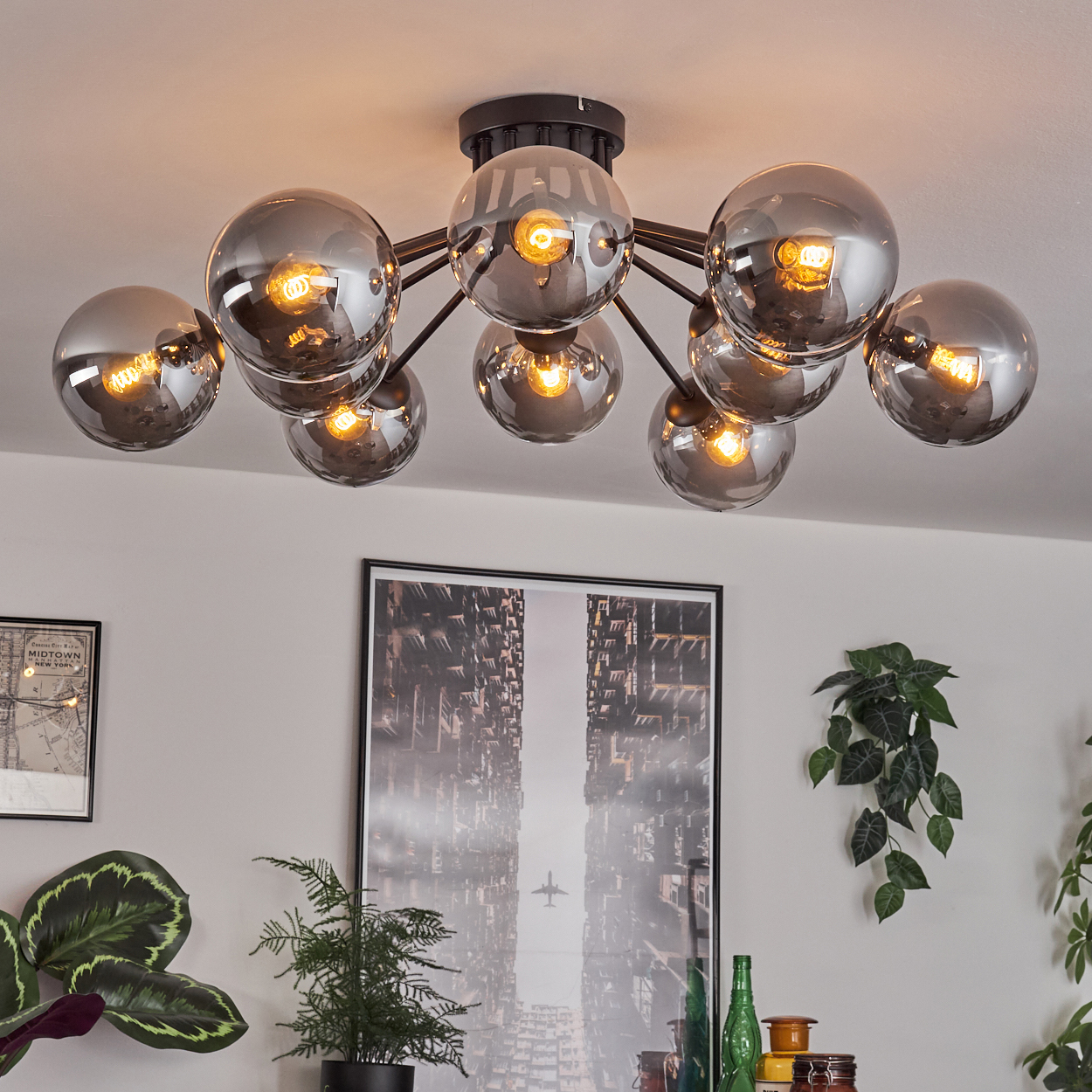 Deckenlampe mit mehreren reflektierenden Kugeln, jede mit einer Glühbirne. Ein gerahmtes Bild und Pflanzen sind im Hintergrund.