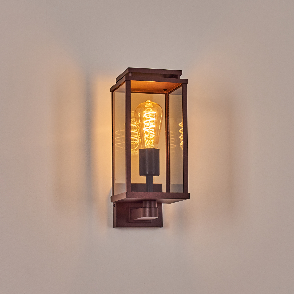 Eine rechteckige Wandleuchte mit einer sichtbaren Edison-Glühbirne. Die Leuchte ist braun, vor einer weißen Wand.