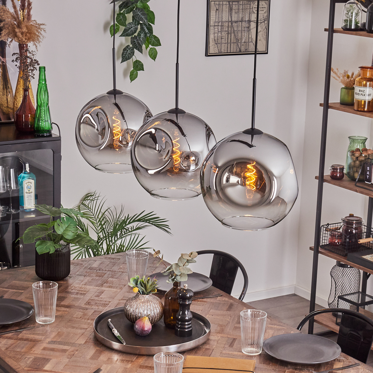 Drei graue Lampen mit einem Wirbel im Inneren. Hintergrund: ein Esstisch mit Essen, Gläsern und anderen Gegenständen.