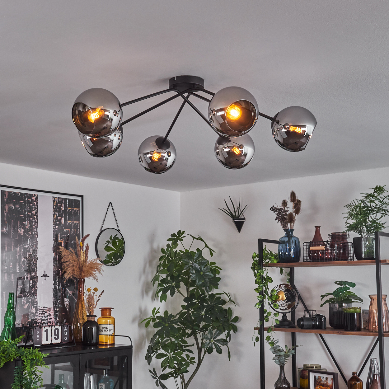 Eine Deckenleuchte mit sechs silbernen Kugellampen in einem Wohnzimmer. Der Raum hat Dekoration und Pflanzen.