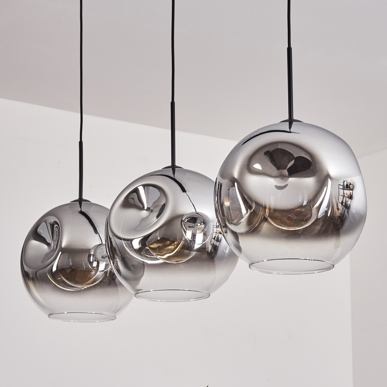 Drei graue Glas-Pendelleuchten mit sichtbaren Glühbirnen hängen vor weißem Hintergrund. Das Design ist minimalistisch.