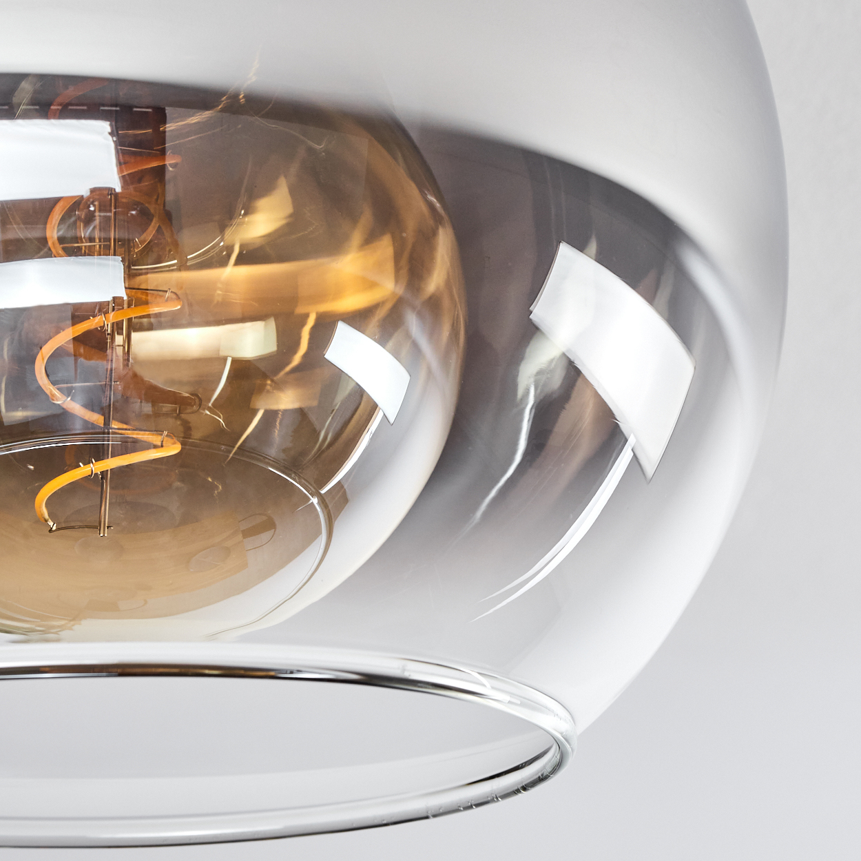 Nahaufnahme einer Glühbirne in einer grauen Glas-Pendelleuchte. Die Details der Glühbirne sind deutlich sichtbar.