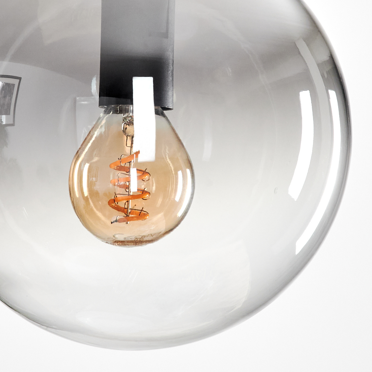 Nahaufnahme einer Glas-Kugel-Pendelleuchte mit einer Wendelglühbirne. Die Kugel ist transparent und die Glühbirne orange.