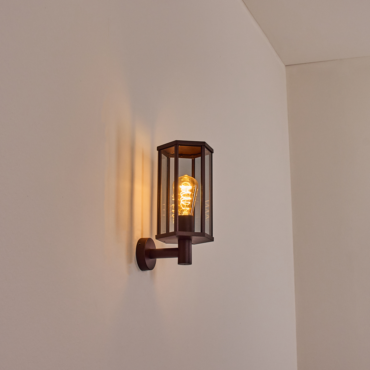 Eine Wandleuchte mit leuchtendem Leuchtmittel, an einer Wand montiert, wirft Licht nach unten. Die Lampe hat einen braunen Rahmen.