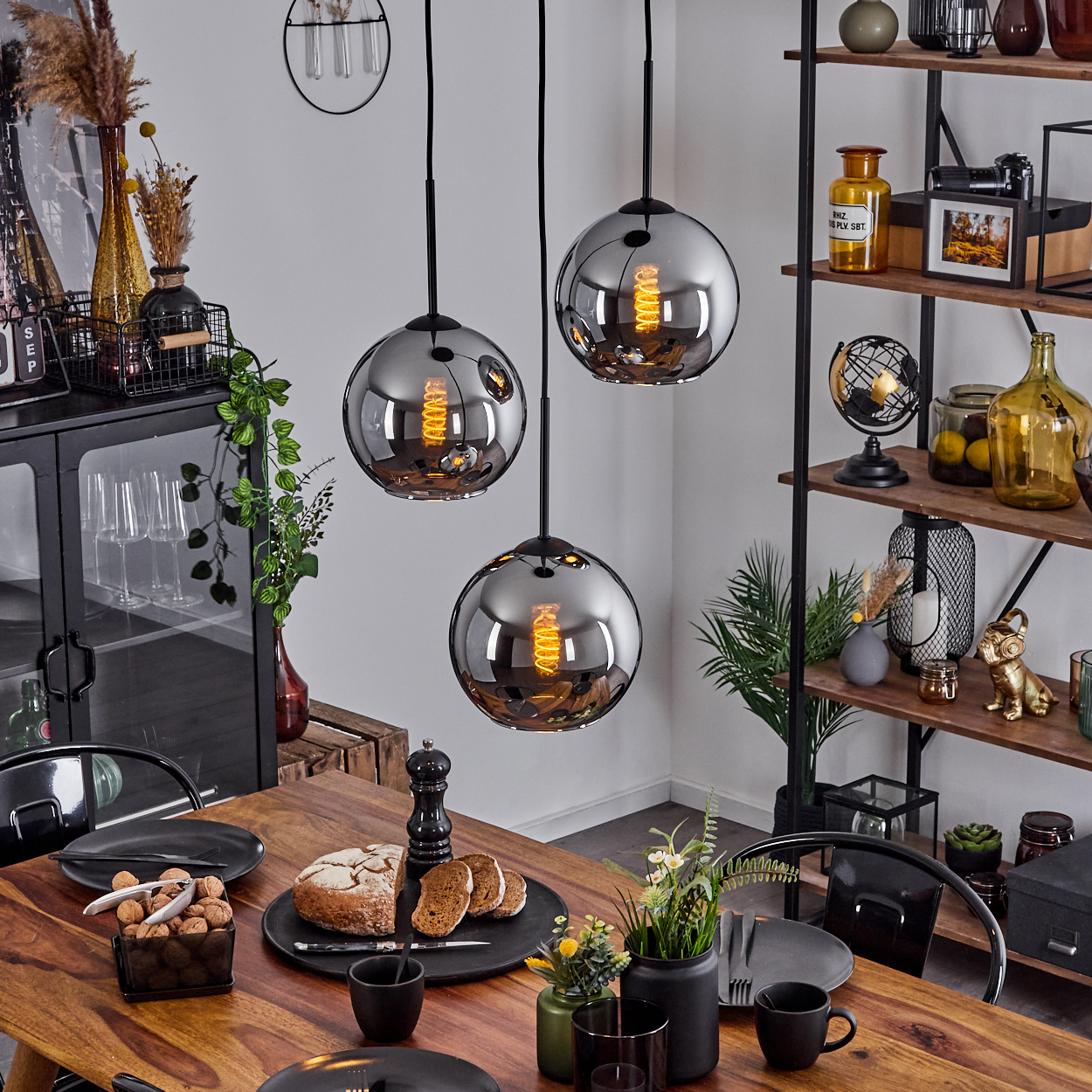 Esszimmer mit drei Pendelleuchten und einem Tisch mit Essen. Regale mit Dekorationen im Hintergrund.