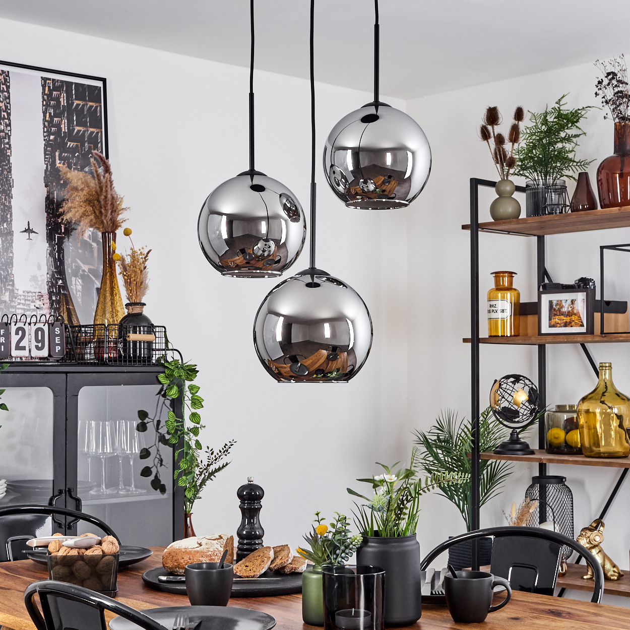 Esszimmer mit drei Pendelleuchten, Esstisch mit Essen. Regale und ein Kalender im Hintergrund.