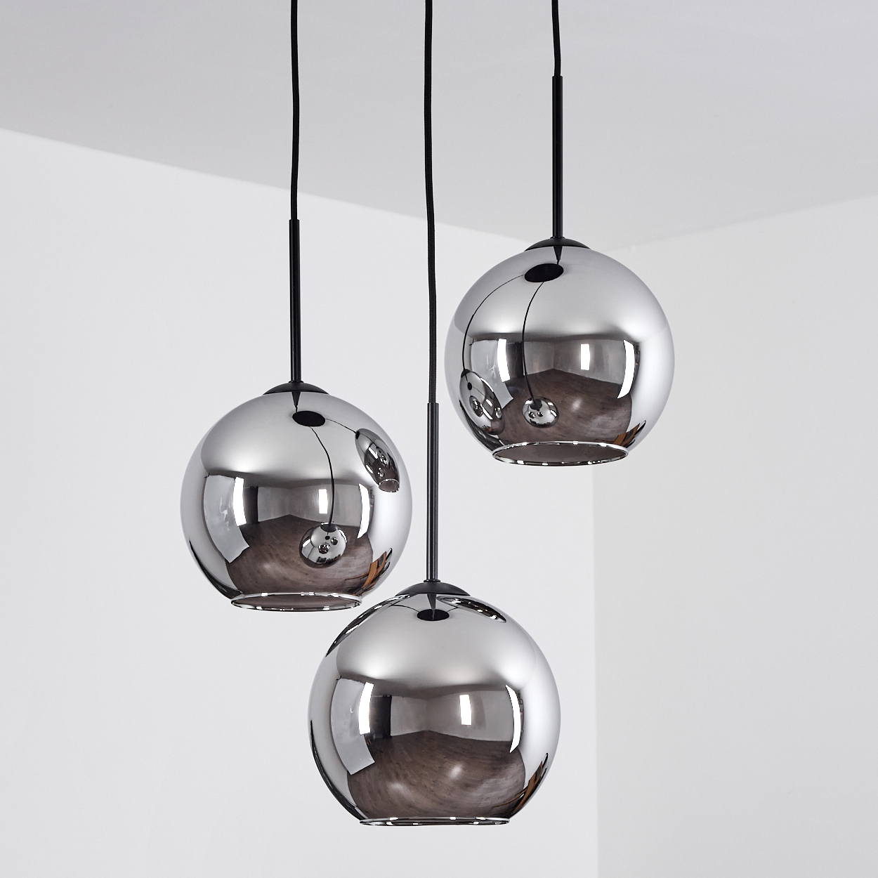 Drei hängende, kugelförmige, verchromte Leuchten reflektieren den Raum. Schwarze Kabel verbinden sie mit der Decke.