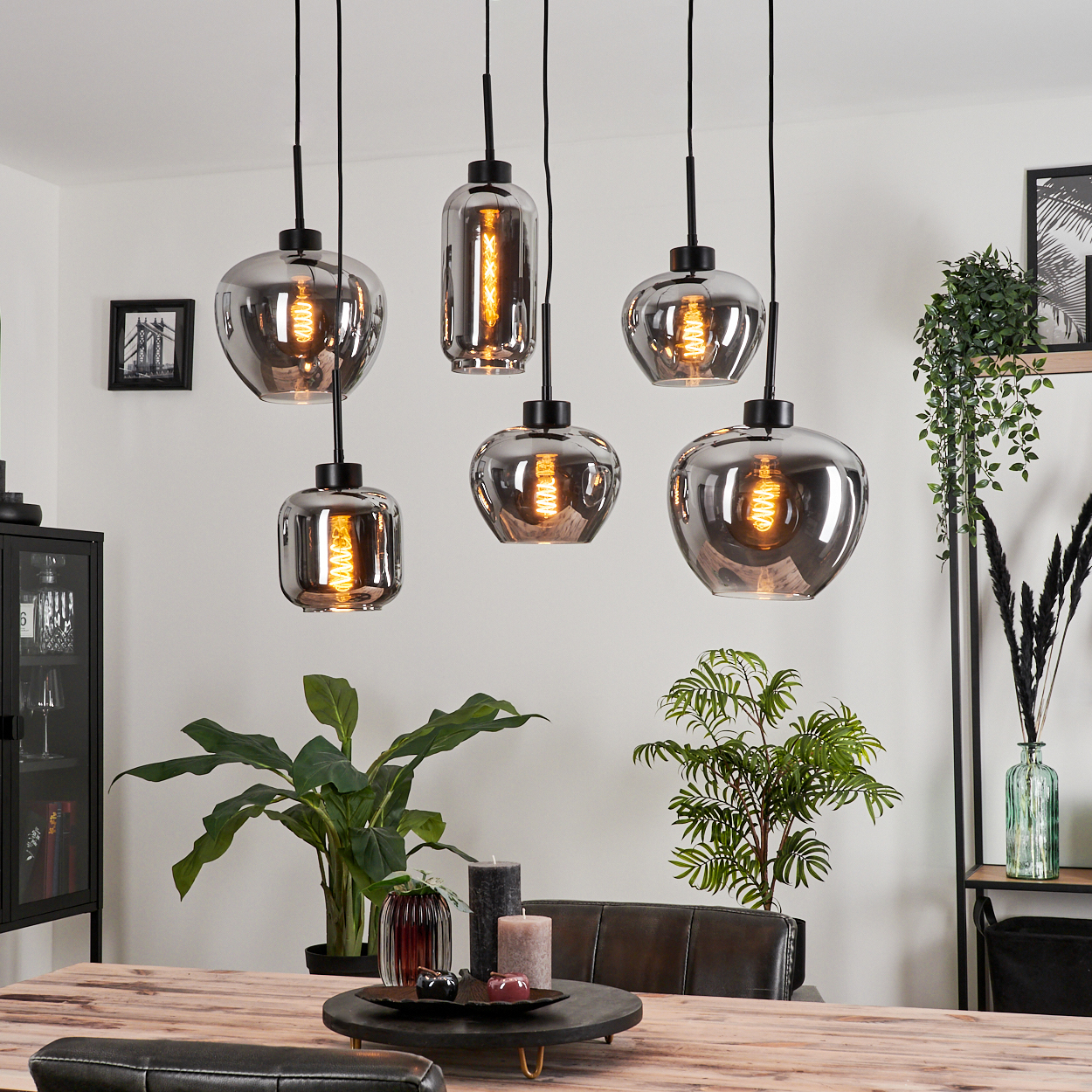 Sechs Hängelampen mit sichtbaren Glühbirnen. Die Lampen haben unterschiedliche Formen und sind über einem Tisch.