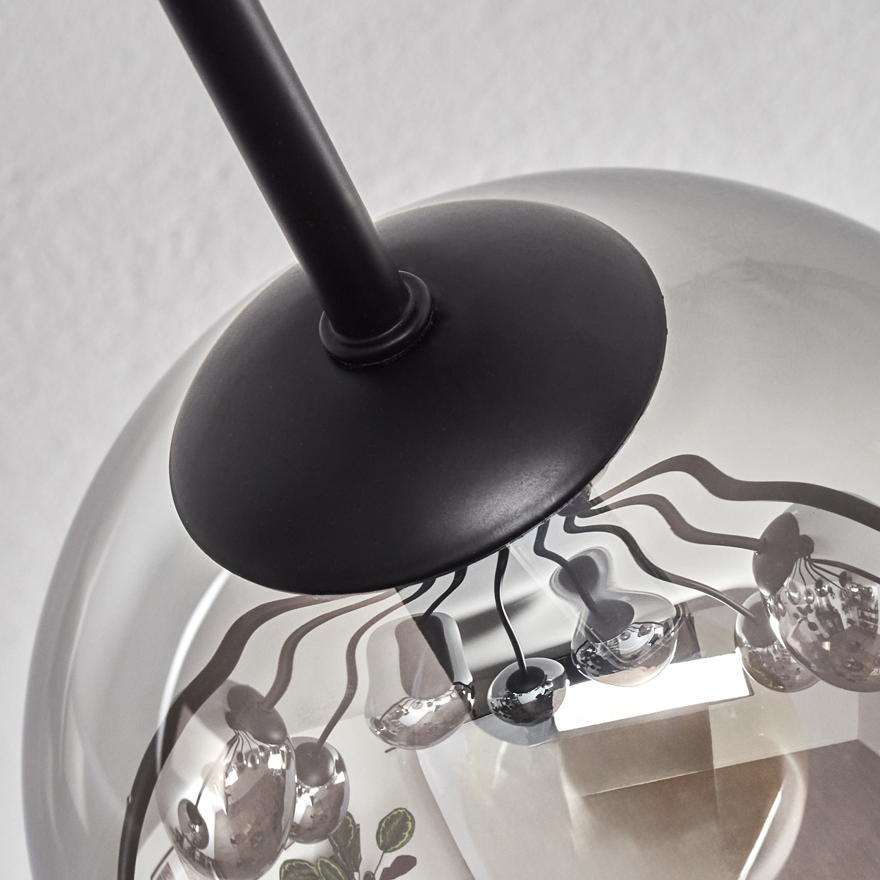 Nahaufnahme einer modernen Deckenleuchte. Ein schwarzer Metallarm und ein Glasschirm sind sichtbar. Der Hintergrund ist weiß.