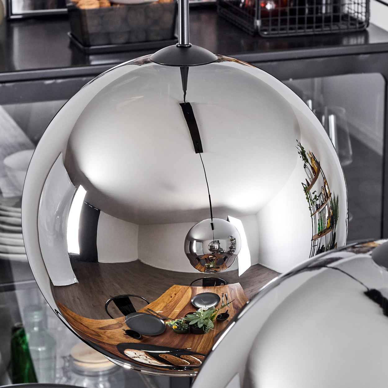 Nahaufnahme einer kugelförmigen, verspiegelten Leuchte, die einen Essbereich reflektiert. Ein Holztisch ist sichtbar.