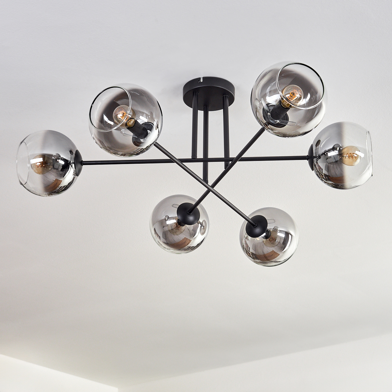 Deckenleuchte mit sechs kugelförmigen, rauchfarbenen Glasschirmen. Schwarze Stangen und eine zentrale Halterung.