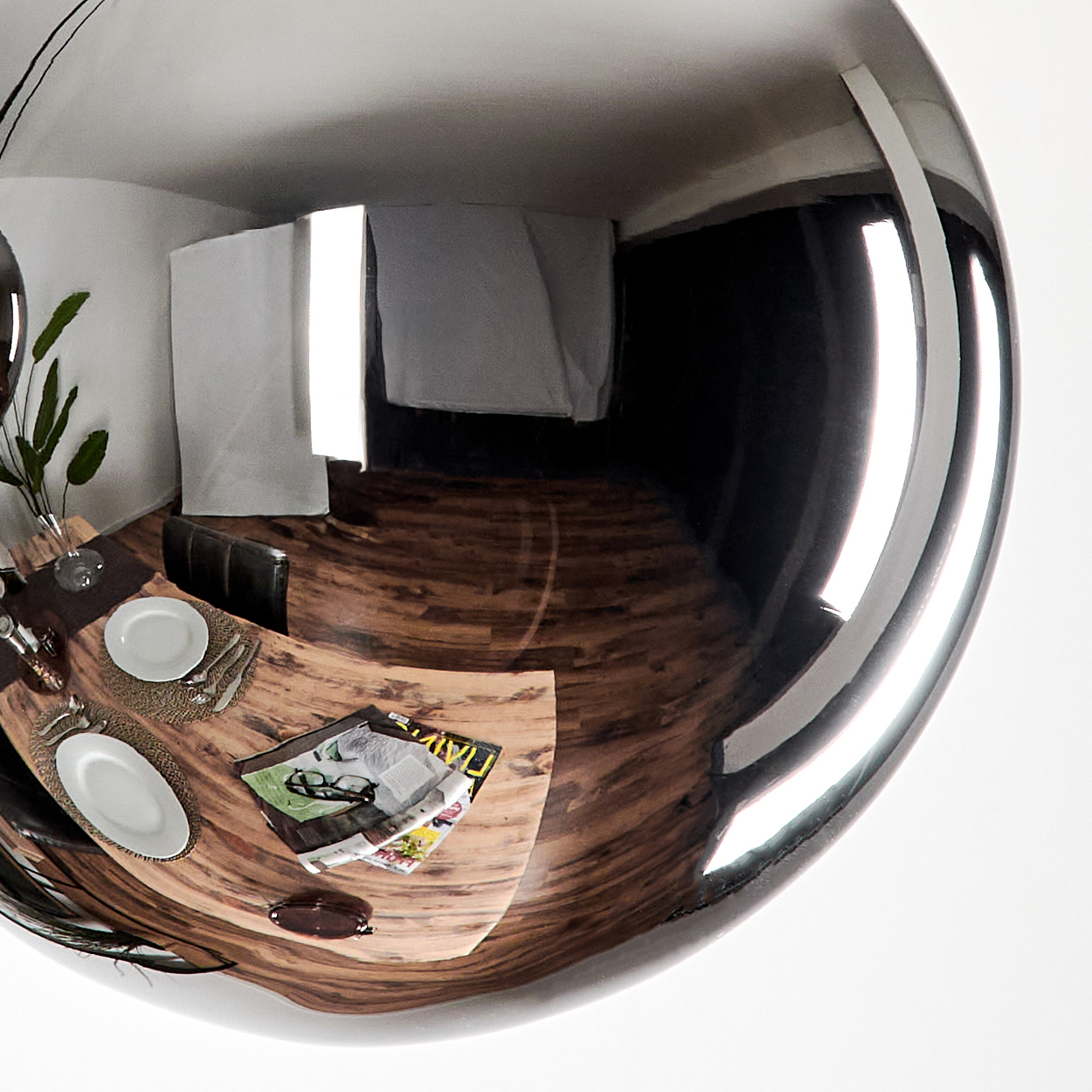 Reflektierende Kugel, spiegelt ein Esszimmer mit Holztisch, Tellern und Zeitschrift. Weiße Wand und Vorhang sichtbar.