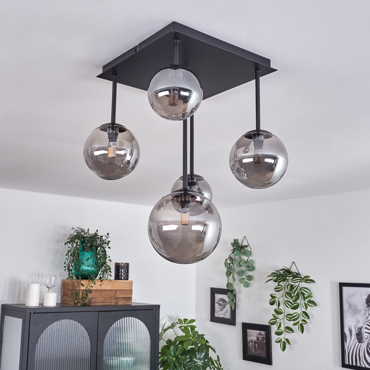 Hängeleuchte mit vier Lichtern und kugelförmigen, rauchfarbenen Glasschirmen. Schwarze Stangen und quadratische Halterung.