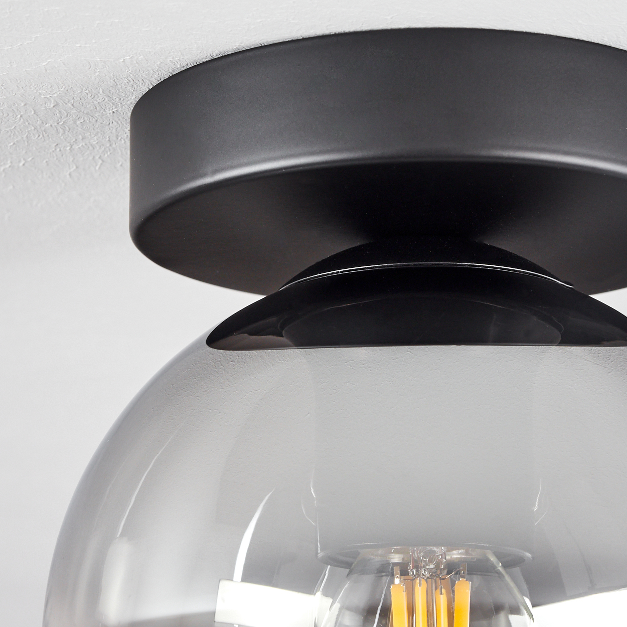 Nahaufnahme einer Deckenlampe. Die Lampe hat einen schwarzen Sockel und eine rauchige Glaskugel mit einer Glühbirne.