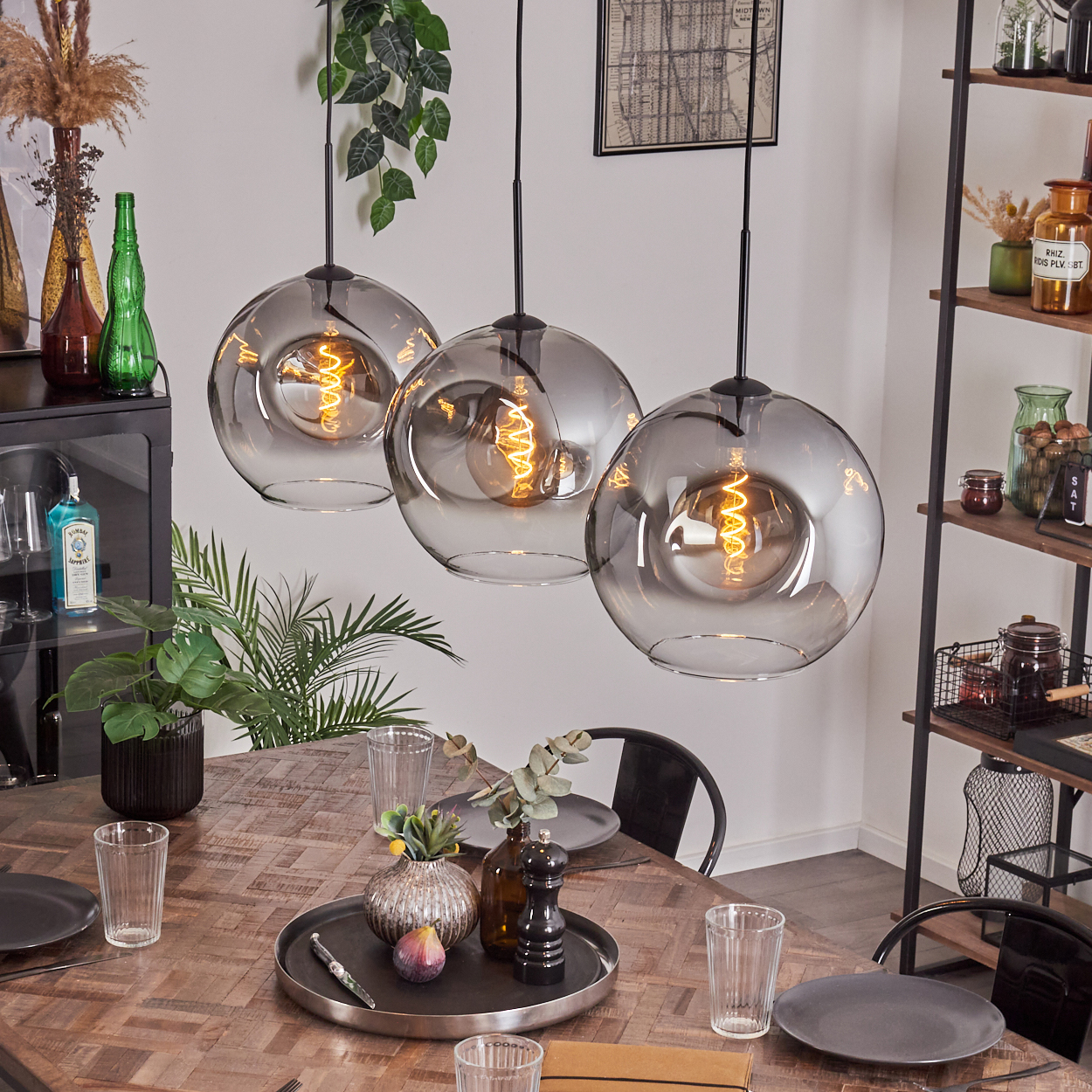Ein Esszimmer mit drei Pendelleuchten, jede mit einem grauen Globus. Ein Tisch ist mit Dekor gedeckt.