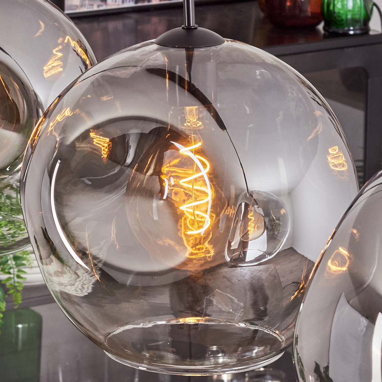 Nahaufnahme einer Pendelleuchte mit sichtbarer Glühbirne in einem reflektierenden Glasschirm. Raumumgebung.