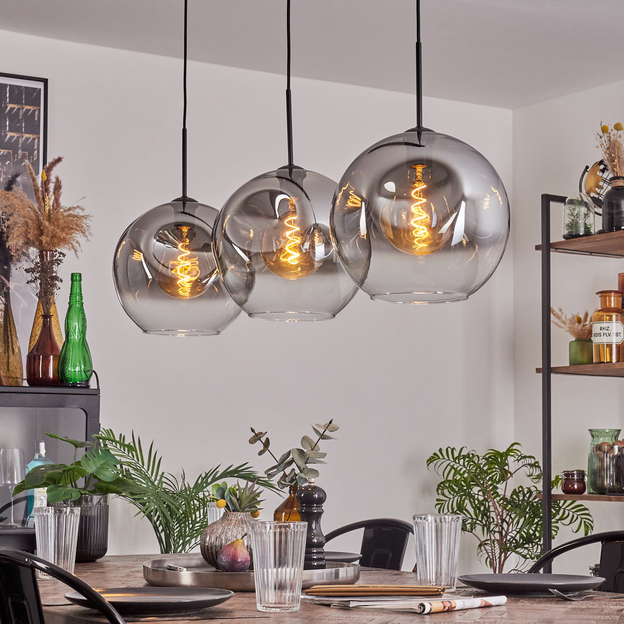 Drei Pendelleuchten mit sichtbaren Glühbirnen hängen über einem Tisch. Raumumgebung mit Dekoration.