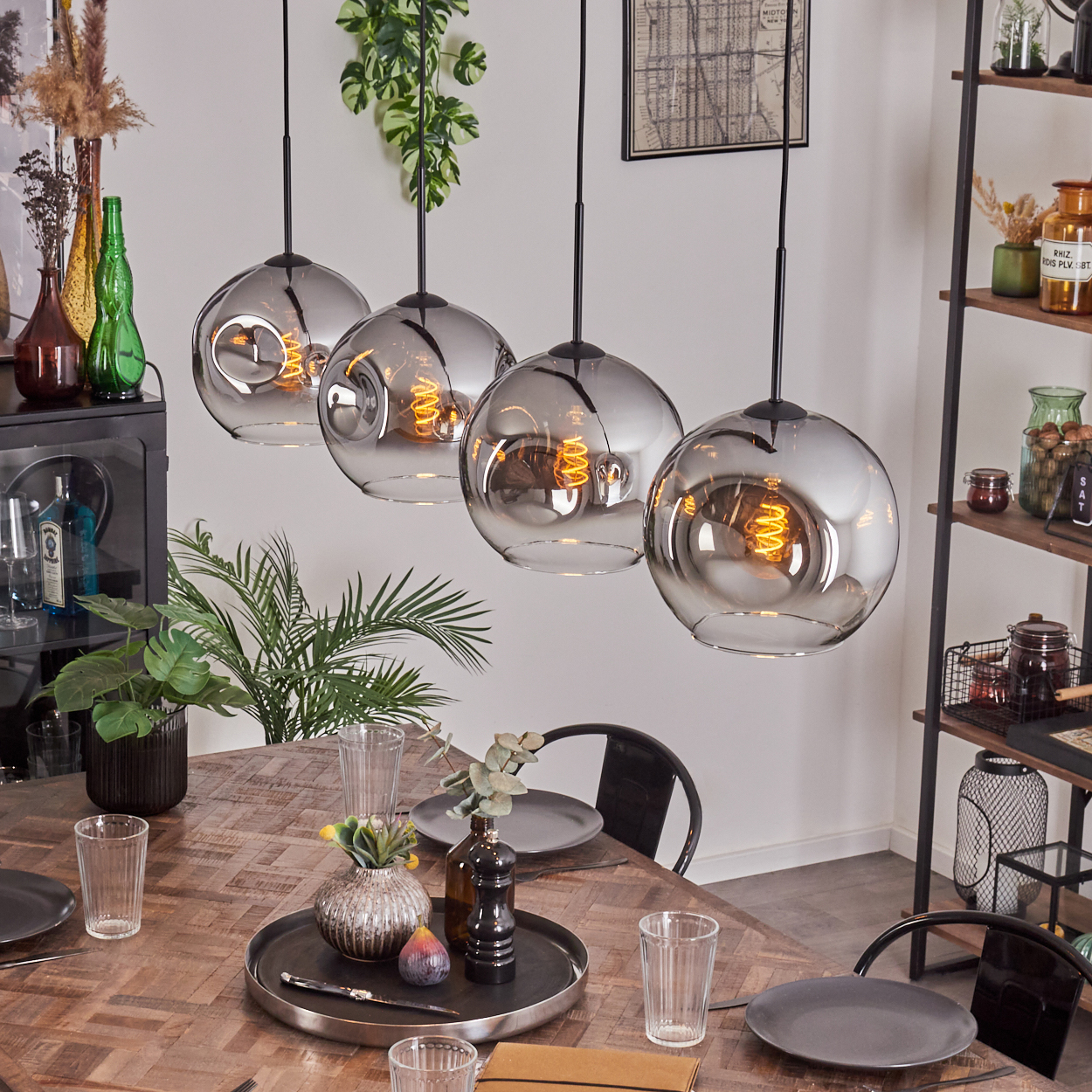 Ein Esszimmer mit vier Hängelampen mit Glaskugeln, einem Holztisch und Pflanzen.