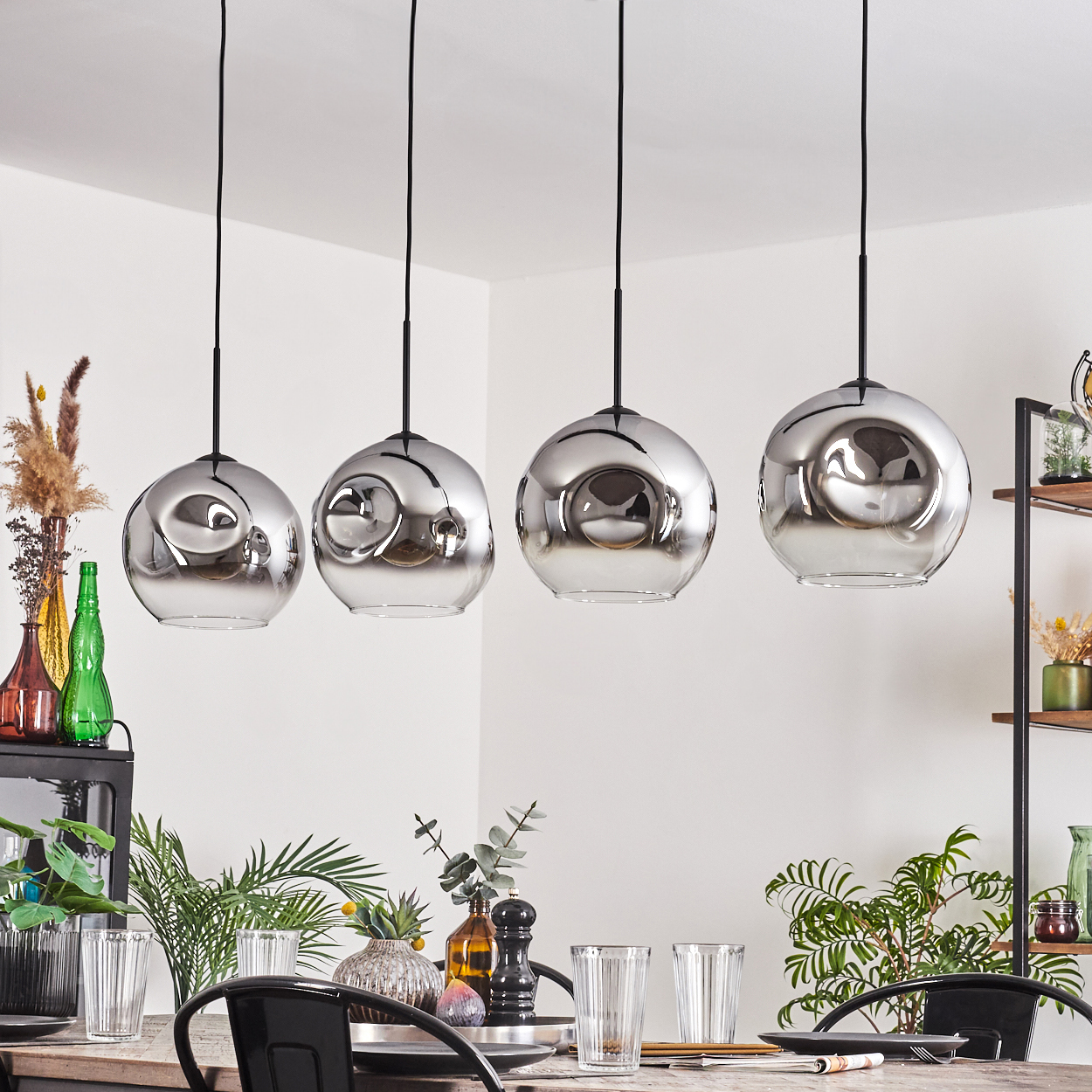 Ein Esszimmer mit vier Hängelampen mit Glaskugeln, einem Holztisch und Pflanzen.
