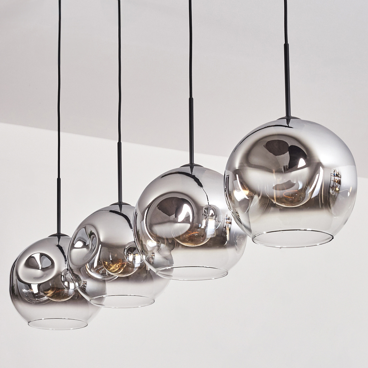 Vier Pendelleuchten mit reflektierenden Glasschirmen hängen von der Decke. Weißer Hintergrund.