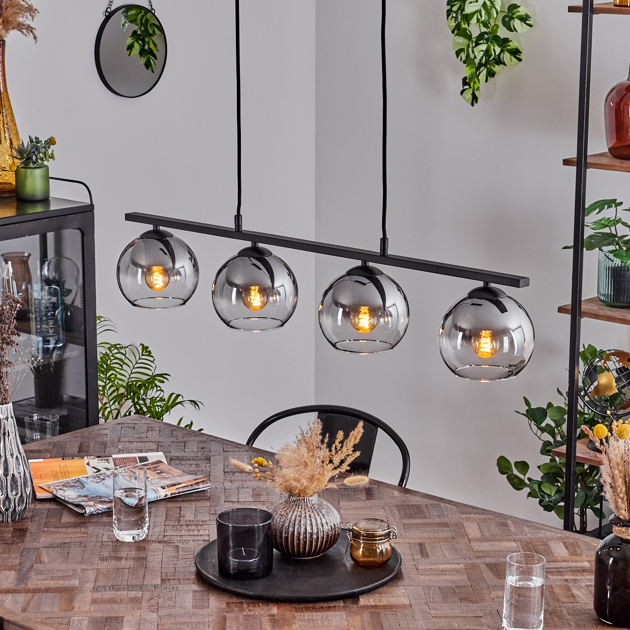 Esszimmer mit Holztisch, schwarzer Lampe mit vier Glaskugeln und Pflanzen.