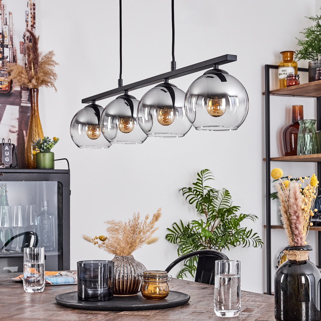 Esszimmer mit Holztisch und schwarzer Lampe mit vier Glaskugeln und Dekorationen.