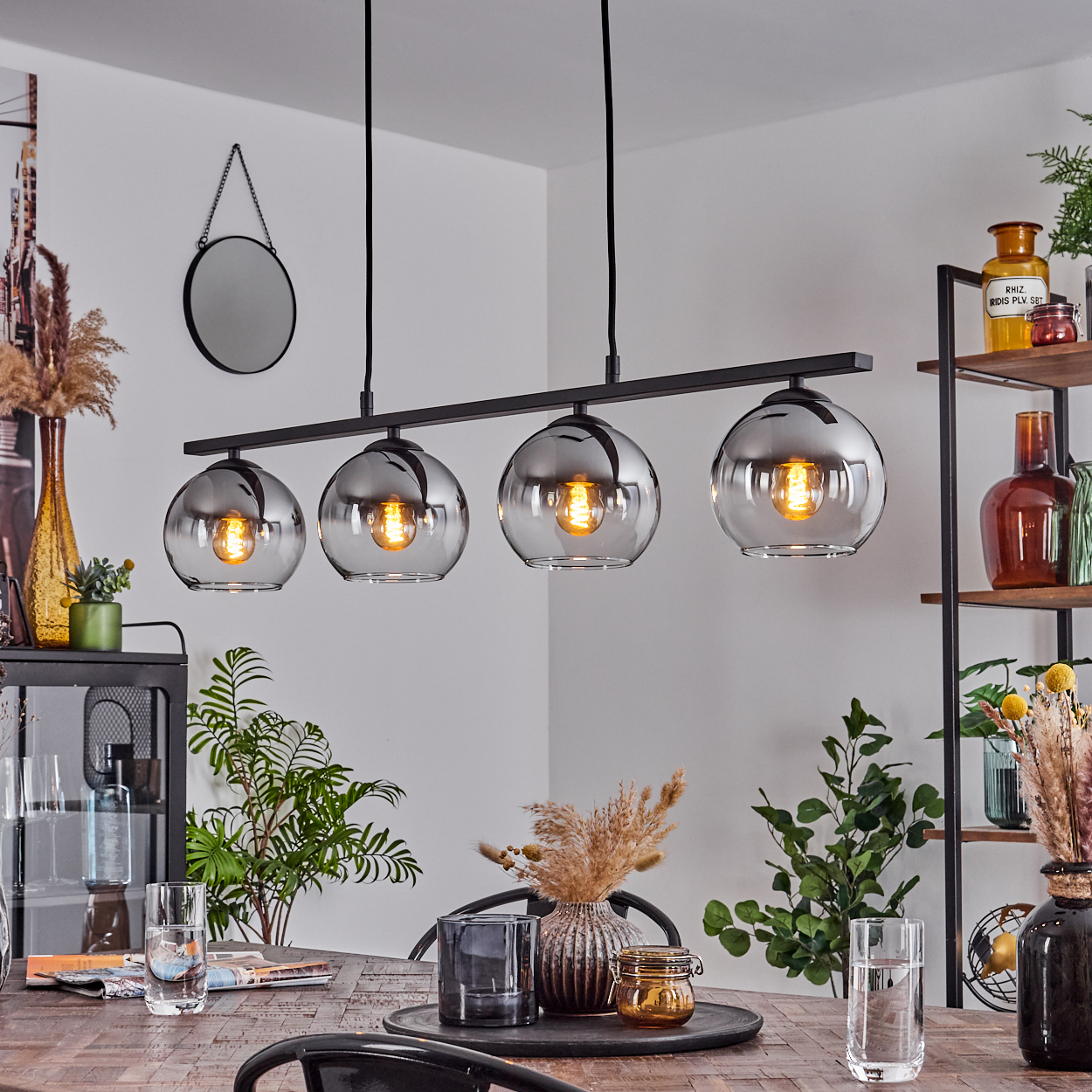 Esszimmer mit Holztisch und schwarzer Lampe mit vier Glaskugeln und Dekorationen.