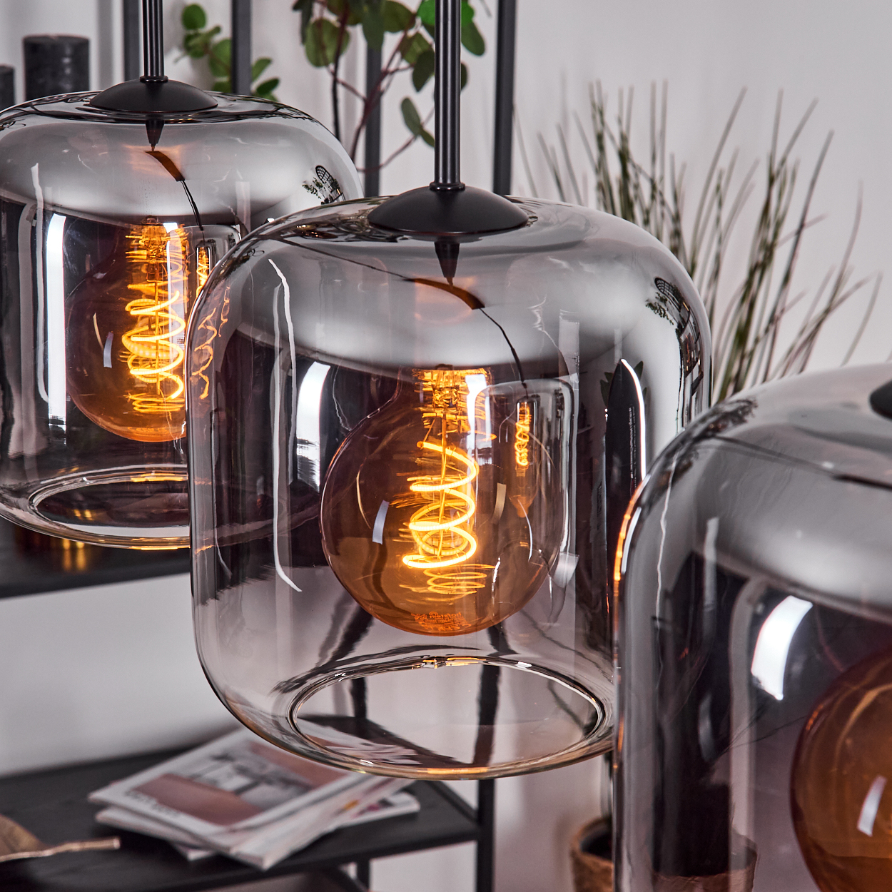 Drei Lampen mit rechteckigem Glasschirm und sichtbarer Glühbirne, mit schwarzem Kabel. Die Lampen sind nah dran.
