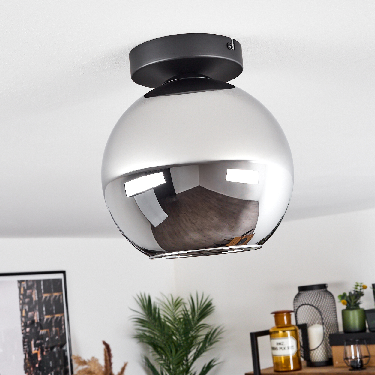 Deckenlampe mit schwarzem Sockel und verspiegeltem, kugelförmigem Glasschirm, der den Raum reflektiert.