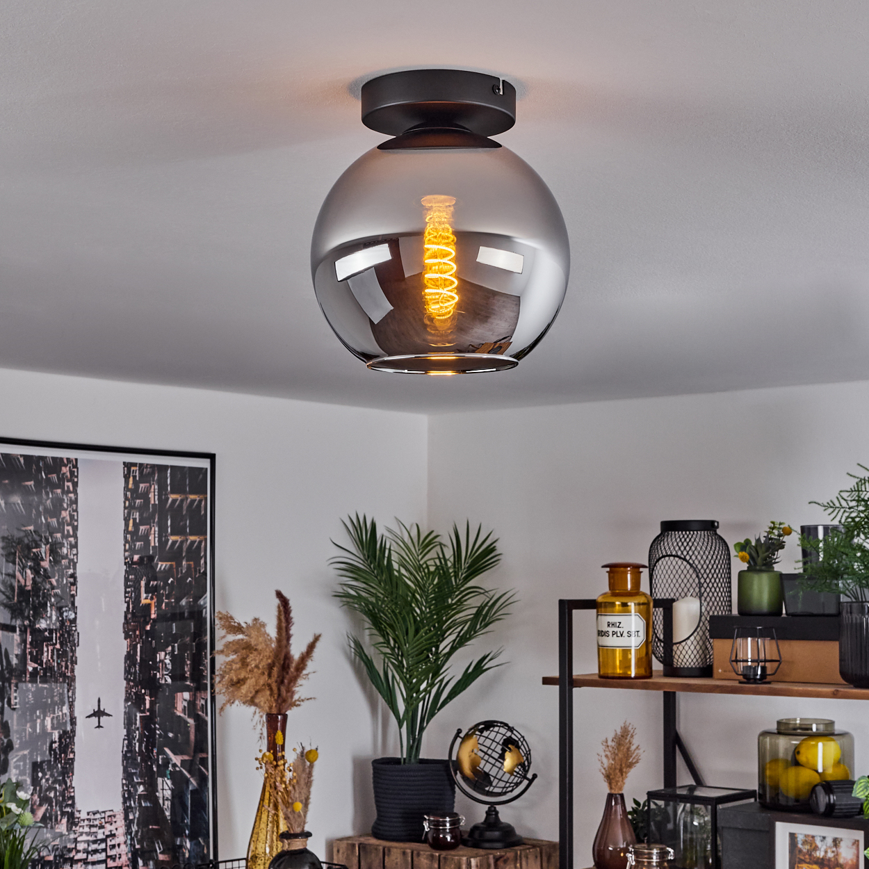 Deckenlampe mit verspiegelter Kugel und brennender Glühbirne, die den Raum mit Pflanzen und Dekorationen reflektiert.