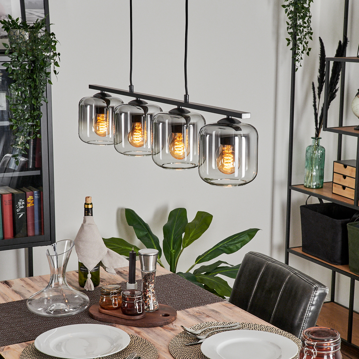 Ein Esszimmer mit Holztisch. Über dem Tisch hängt eine lineare Lampe mit vier Glasschirmen, je mit Glühbirne.