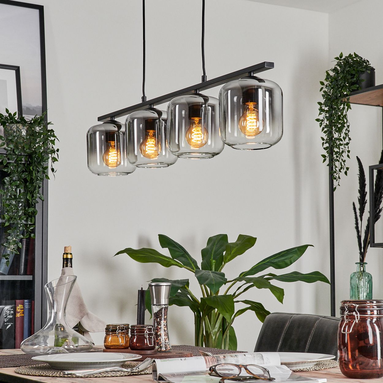 Vier Pendelleuchten mit grauem Glas. Warme Lichter sind an. Esszimmer mit schwarzem Dekor und Möbeln.