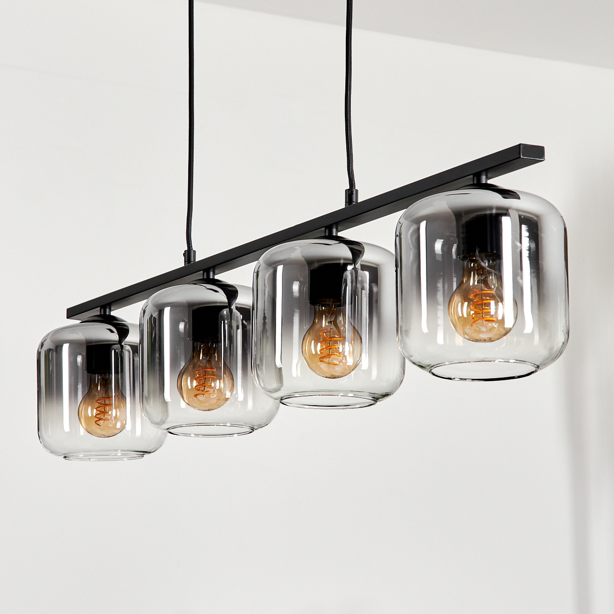 Eine lineare Lampe mit vier Glasschirmen, je mit einer Glühbirne. Die Lampe hängt von der Decke.