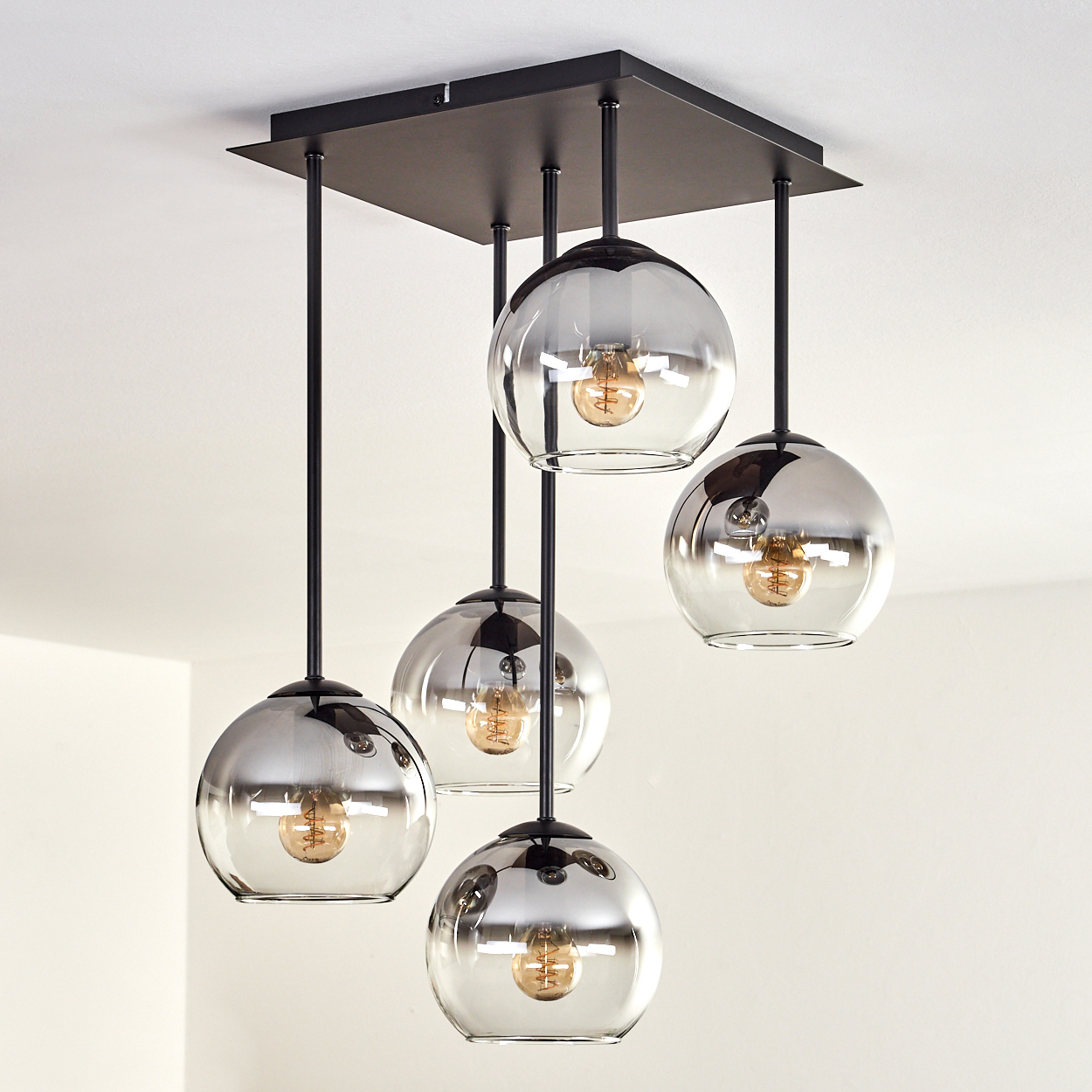 Deckenlampe mit fünf Glaskugelschirmen, jede mit einer sichtbaren Glühbirne, von der Decke hängend.