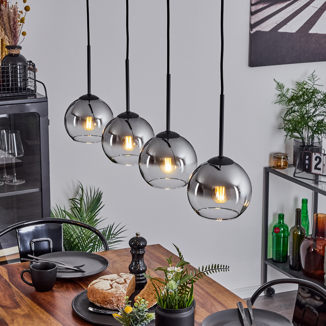Esszimmer mit Tisch, vier Hängelampen. Jede Lampe ist kugelförmig mit sichtbarer Glühbirne.