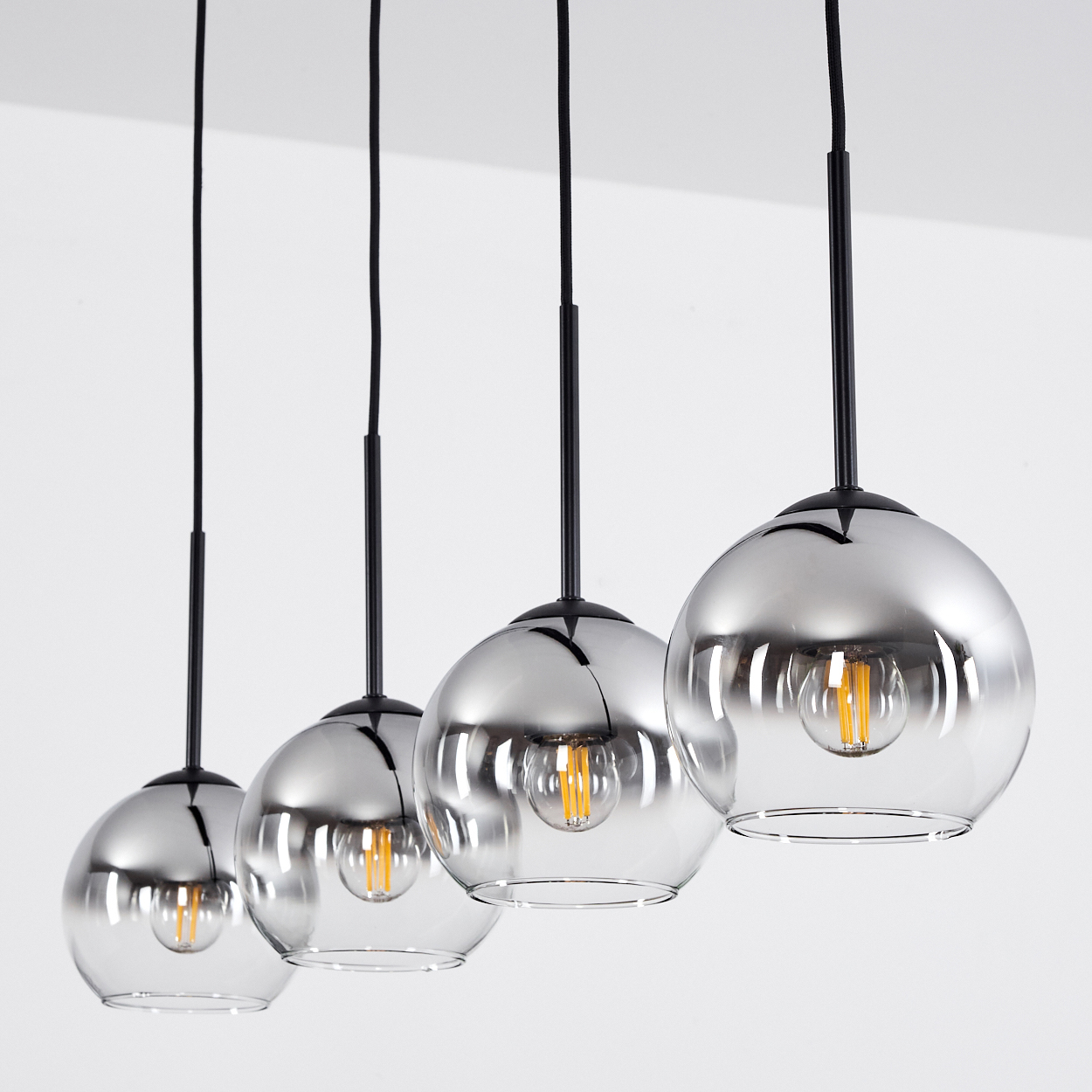 Vier kugelförmige Lampen hängen von der Decke. Jede Lampe hat eine sichtbare Glühbirne. Weißer Hintergrund.