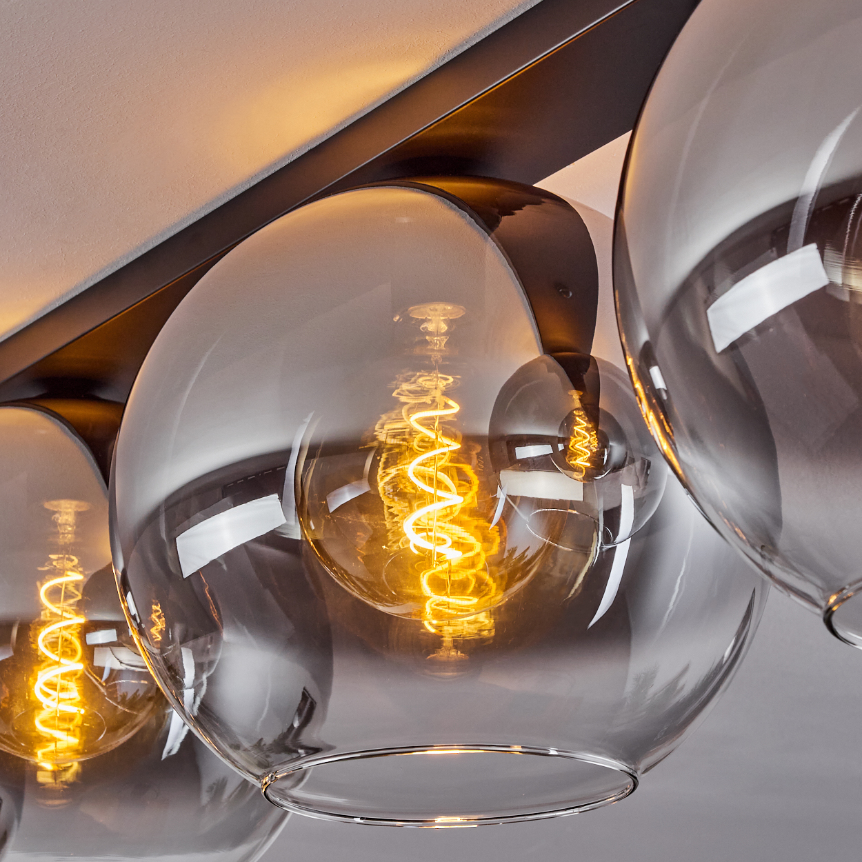 Nahaufnahme einer Glühbirne in einer klaren, kugelförmigen Lampe, montiert an einem schwarzen Balken, helles Licht.