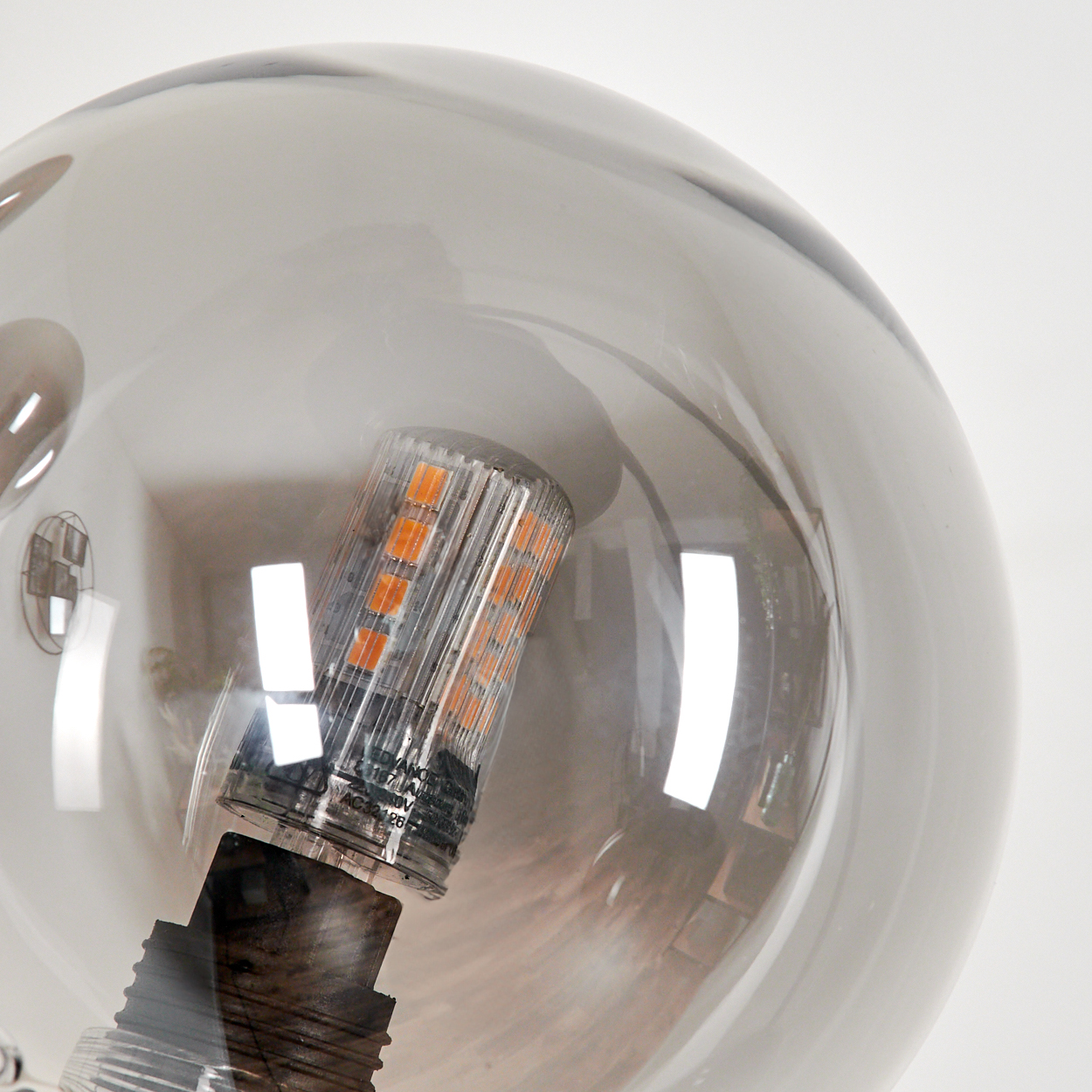 Nahaufnahme einer Glühbirne in einer kugelförmigen Lampe. Die Lampe hat eine klare, reflektierende Oberfläche. Weißer Hintergrund.