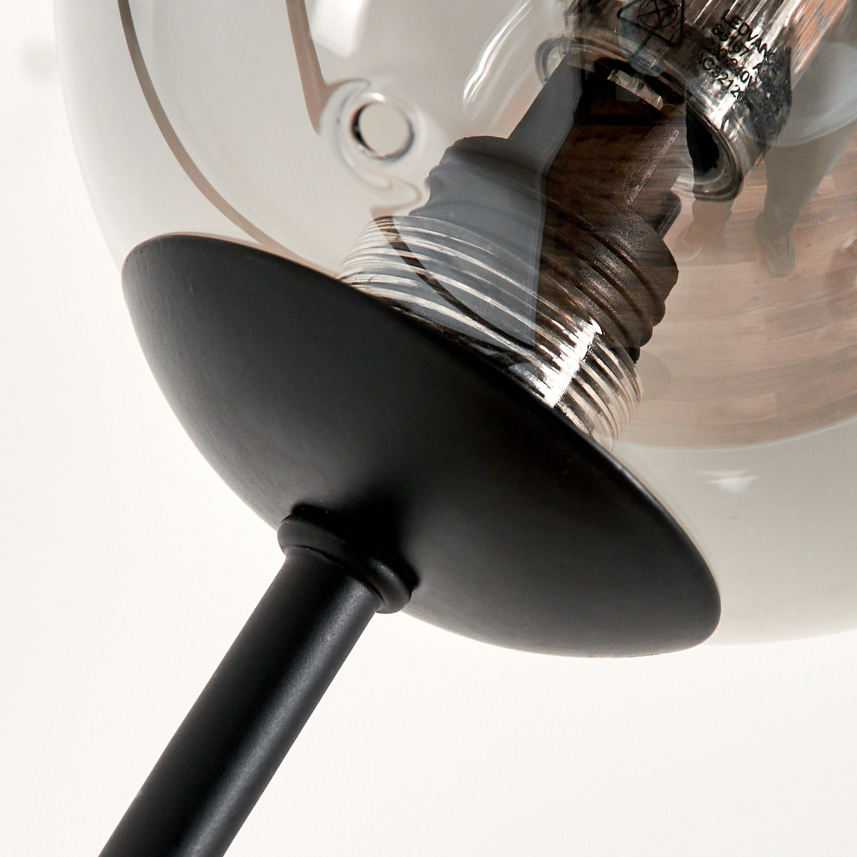 Nahaufnahme einer Pendelleuchte aus Rauchglas mit einer sichtbaren Glühbirne im Inneren.