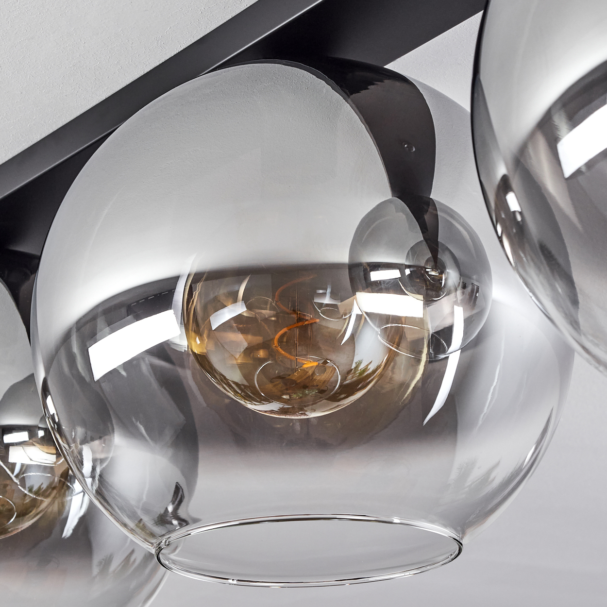 Nahaufnahme einer Deckenlampe mit vier kugelförmigen Schirmen. Jeder enthält eine Glühbirne. Die Schirme sind klar.