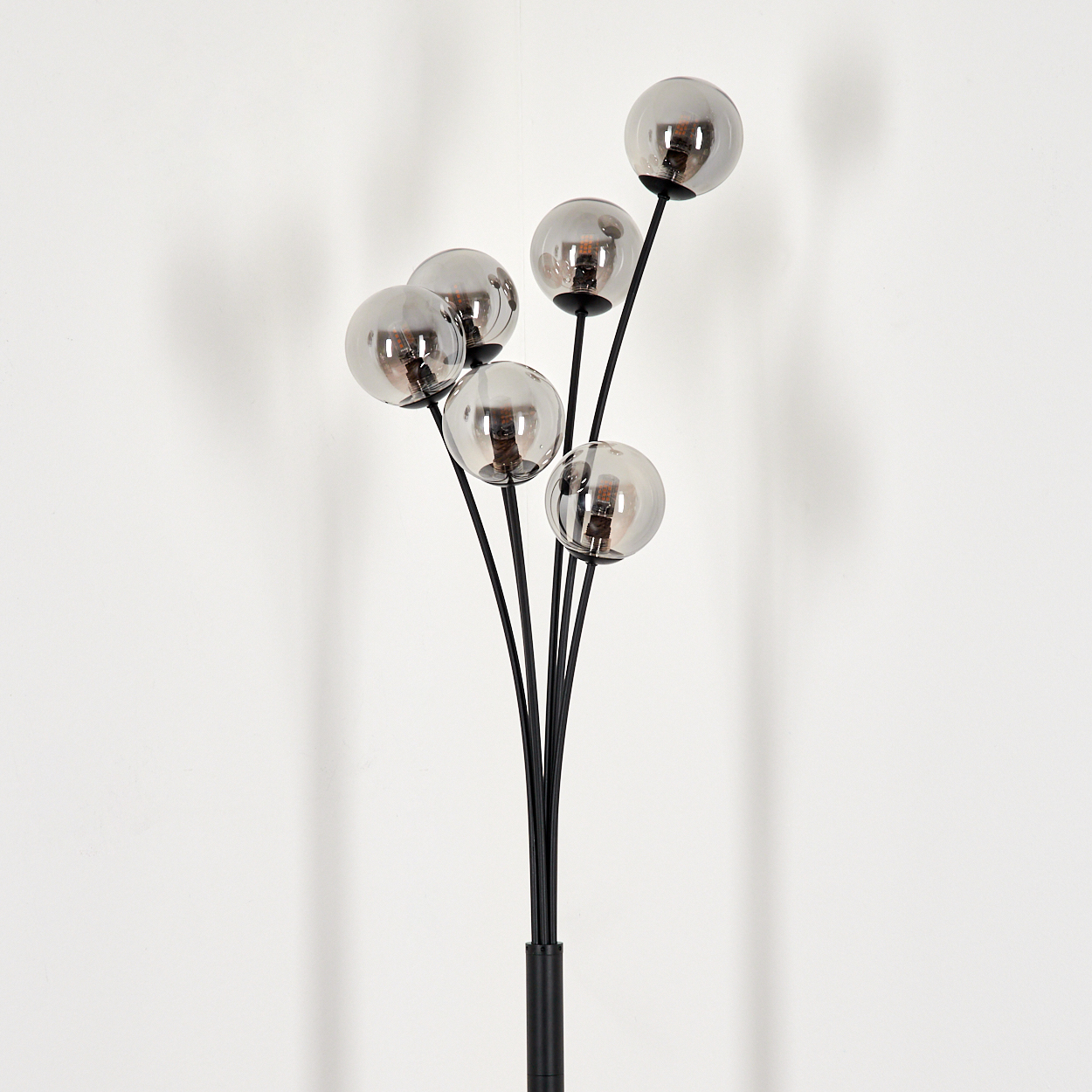 Stehleuchte mit sechs Chrom-Globus-Schirmen. Die Lampe hat einen schwarzen Sockel und Stiel, vor weißer Wand.
